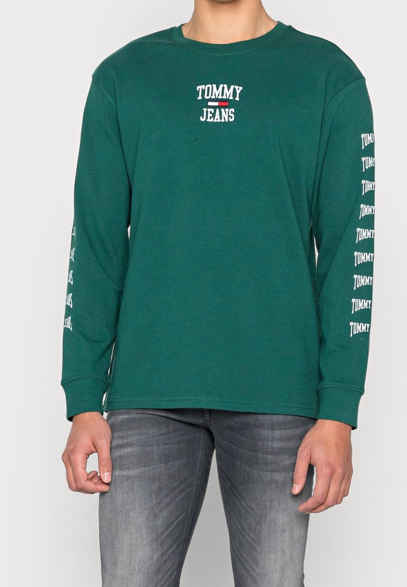 Vihreä pitkähihainen t-paita pyöreällä kaula-aukolla, jossa rinta- ja hihoissa valkoinen "TOMMY JEANS" -teksti. Valmistettu puuvillasekoitteesta.