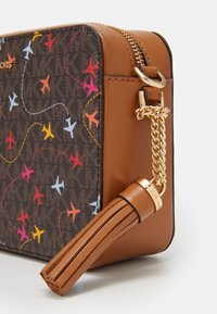 Borsa in pelle marrone con motivi colorati di aerei sulla parte anteriore, hardware in catena dorata e dettaglio con frange. Chiusura con zip sulla parte superiore.