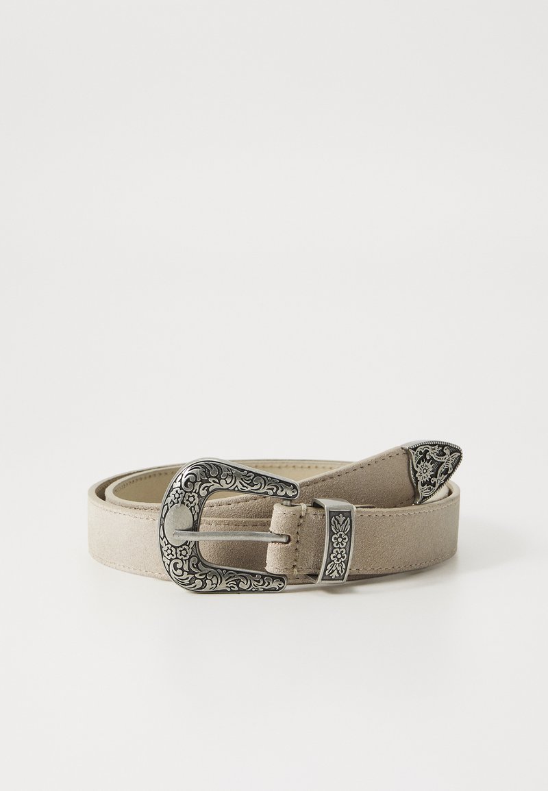 Beige mockaskärp med en utsmyckad silverfärgad spänne, som har blommiga gravyrer och spetsig topp. Platt design med minimal textur.