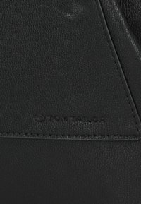 Crna teksturirana kožna površina s urezanim "Tom Tailor" logotipom, s kontrastnim šavovima duž ruba i elegantnim geometrijskim dizajnom.