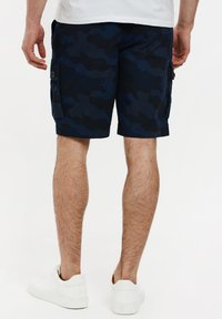 Marineblå cargoshorts med et tekstureret camouflage mønster, sidelommer og en afslappet pasform, parret med hvide sneakers.