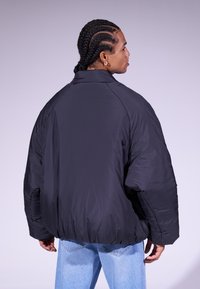 Casaco puffer preto com gola alta, corte oversized e punhos elásticos. O tecido parece suave com um acabamento mate.