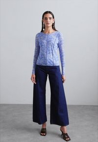 Ανοιχτό μπλε μπλουζάκι με μακριά μανίκια και λουλουδάτο σχέδιο, συνδυασμένο με σκούρες φαρδιές τζιν. Το μοντέλο φορά καφέ ανοιχτά ψηλοτάκουνα και κρεμαστά σκουλαρίκια.