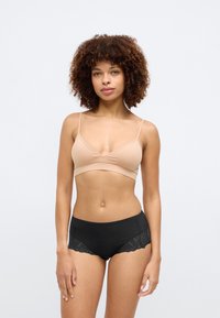 Beige bralette med v-udskæring og tynde stropper, parret med sorte shorts med blonder på kanterne. Glatte teksturer.
