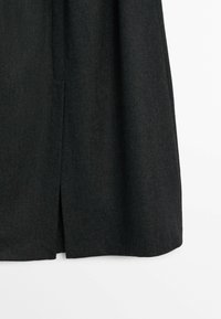 Jupe gris foncé en tissu à texture lisse, dotée d'une fente latérale pour faciliter les mouvements et d'un design épuré et simple.