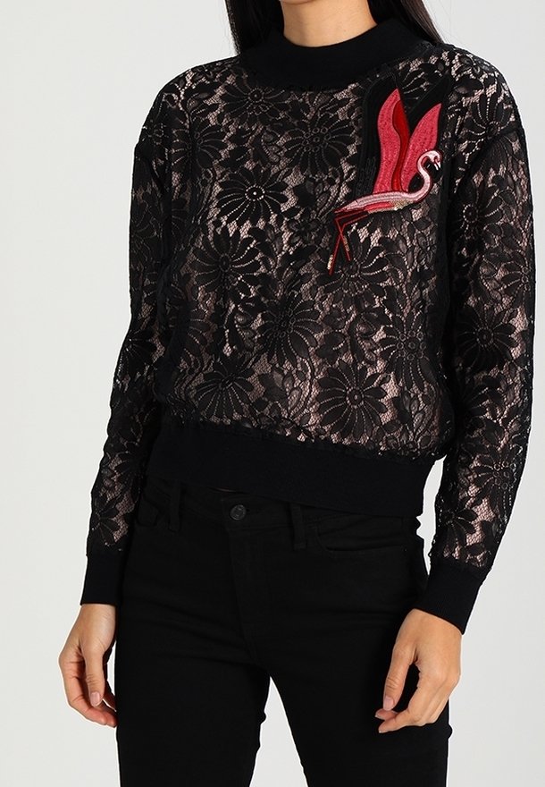 Pull en dentelle noire avec un motif floral, col côtelé et un accent flamant rose brodé en rouge sur le côté gauche de la poitrine. Manches longues, ajusté.