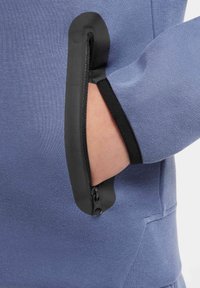 Sweatshirt bleu avec une poche zippée dotée d'une bordure noire, texture lisse et design ergonomique pour un accès facile.