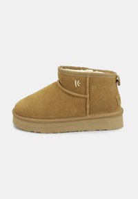 Stivaletto in suede color tan con una fodera morbida, punta rotonda e cuciture minime. Presenta un piccolo logo sul lato e una suola in gomma testurizzata.
