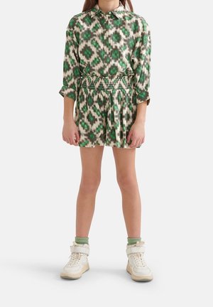 Vestido con patrón verde y beige, con cuello tipo solapa y cintura ajustada, combinado con zapatillas blancas y calcetines verdes.