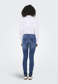 Jeans skinny de mezclilla azul con cintura alta, diseño de cinco bolsillos y un leve desvanecimiento. Combinados con una camisa blanca de cuello y zapatillas.