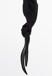 Écharpe noire en tissu léger et texturé, avec un design en torsade nouée. Les extrémités sont allongées et légèrement effilochées.