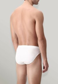 Pannolini bianchi in cotone con una texture liscia e una cintura elastica, mostrati da dietro su uno sfondo neutro.