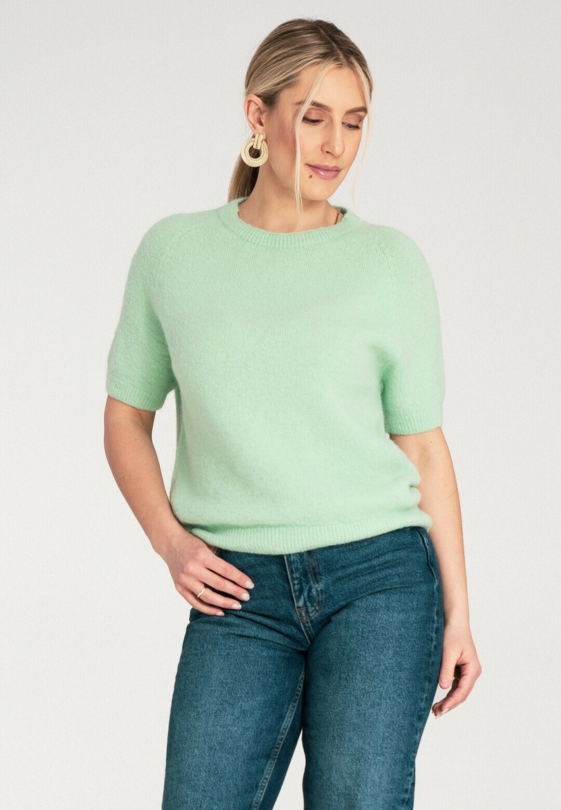 Miętowa krótko rękawowa sweter w miękkiej, puszystej teksturze z prążkowanym dekoltem i dołem. W połączeniu z niebieskimi dżinsami.