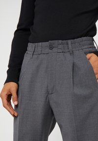 Grau gestreifte Hose mit Faltendesign, elastischem Bund und Knopfverschluss. Aus strukturiertem Stoff gefertigt, mit seitlichen Taschen.