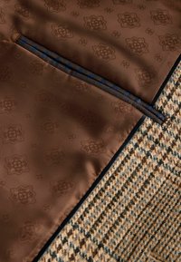 Brūns rakstains audums ar smalku ziedu dizainu, papildināts ar pinētu zilu akcentu. Blakus esošs teksturēts bēšs un brūns houndstooth raksts.