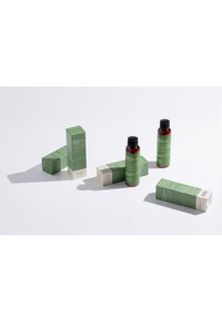 Två mörkröda flaskor med svarta lock omges av gröna och krämfärgade lådor. Lådorna har detaljerad text och en rektangulär form.