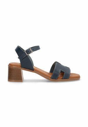 Sandal de cuero azul marino con tacón cuadrado, punta abierta y tira en el tobillo. Presenta acentos cosidos y una plantilla acolchada en color marrón.