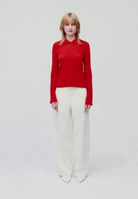 Suéter vermelho de mangas compridas com decote em colarinho, combinado com calças brancas de pernas largas. Tecido elegante e calçado branco de bico.