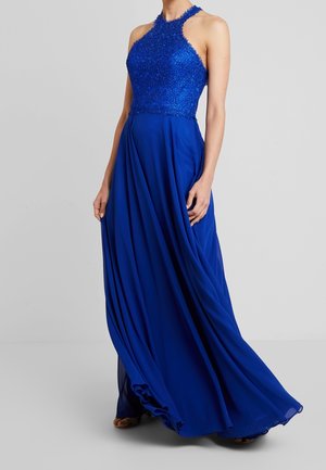Koningsblå aftenkjole i gulvlængde med perlebesat halterhalsudskæring og flydende chiffon nederdel båret af en stående person.