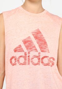 Różowy, bezrękawnik sportowy wykonany z miękkiego materiału, z teksturowanym nadrukiem logo Adidas w ciemniejszym odcieniu różu.