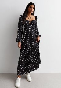 Black pleated dress with white polka dots, puff sleeves, and a keyhole front. Paired with white sneakers. Smooth, lightweight fabric.