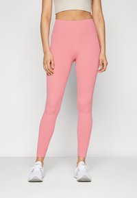 Leggings rosa a coste con vita alta e design aderente, abbinati a scarpe da ginnastica bianche. Texture liscia senza motivi o dettagli visibili.
