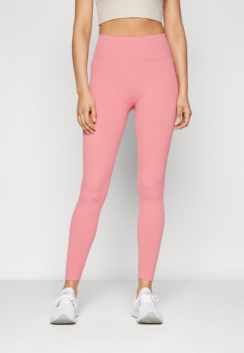 Leggings rosa a coste con vita alta e design aderente, abbinati a scarpe da ginnastica bianche. Texture liscia senza motivi o dettagli visibili.