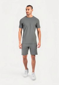 Graues Sport-T-Shirt und Shorts-Set aus glattem, dehnbarem Stoff, mit kurzen Ärmeln und Rundhalsausschnitt, kombiniert mit weißen Turnschuhen.
