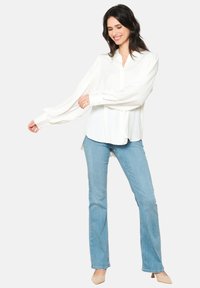 Camicia bianca con bottoni, maniche lunghe e ampie, dal taglio rilassato, abbinata a jeans skinny azzurri e tacchi beige. Tessuto morbido.