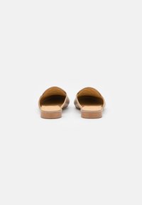 Mule sem costas em couro castanho com acabamento suave, palmilha acolchoada e sola de borracha de cor clara; design minimalista com bordas arredondadas.