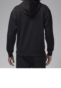 Uomo in felpa nera con cappuccio e pantaloni neri abbinati, visto di spalle su uno sfondo grigio.