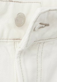 Tissu en denim blanc avec bouton-pression en métal, montrant une taille partiellement ouverte et des détails de couture visibles beige.