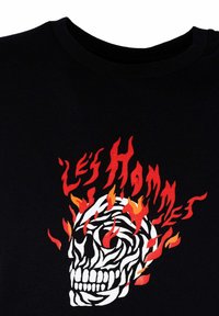 Camiseta de algodón negra con un diseño gráfico de una calavera con franjas y llamas en rojo y naranja, con el texto "Les Hommes."