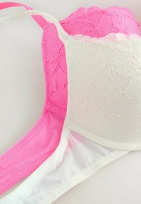 Lingerie weergegeven in roze en wit; heeft een florale kanten overlay, een mesh-textuur, verstelbare banden en een gladde effen band.