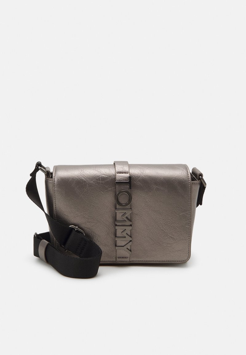 Sac bandoulière argenté avec sangle noire réglable et logo TOMMY vertical sur le rabat avant sur fond blanc.