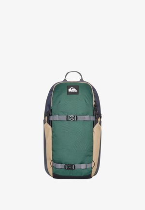 Grüner und beiger Rucksack aus strukturiertem Stoff, mit verstellbaren Trägern, Seitentaschen und einem Logo-Patch an der Vorderseite.