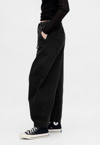 Pantaloni in denim neri oversize con cintura elastica e cordoncino. Presentano tasche frontali e una finitura testurizzata. Abbinati a sneaker nere.