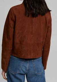 Bruine suede jacket met een cropped ontwerp, met een gladde textuur en minimale stiksels, gecombineerd met blauwe denim jeans.