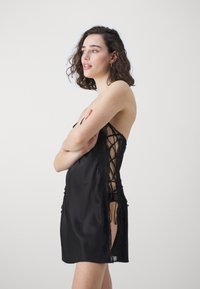 Black satin dress with lace detailing, featuring a crisscross back and high side slits, showcasing a smooth texture and elegant design.