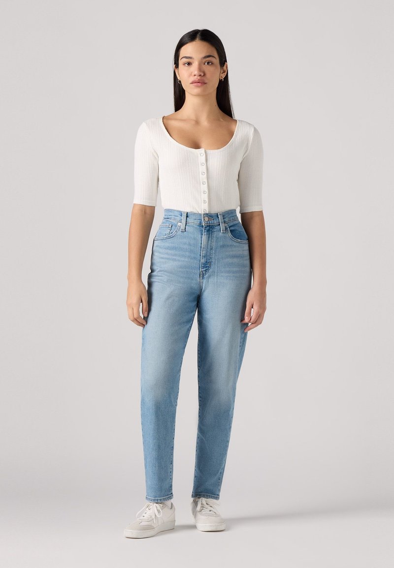 Weißes geripptes Kurzarmoberteil mit Knopfleiste, kombiniert mit hoch taillierten, hellblauen, geraden Jeans und weißen Sneakern.