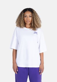 Hvit oversized t-skjorte med senkede skuldre, med blå grafisk tekst "ONE EARTH" på øvre venstre del. Myk bomullsstoff.