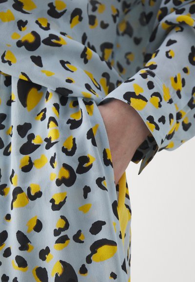 Material textil albastru cu un model de leopard în negru și galben, având o textură moale și o croială lejeră. Include un detaliu de buzunar pe lateral.