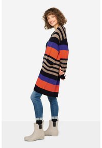 Randig lång kofta i marinblått, orange och lila, tillsammans med blåjeans och beige ankelskåpor. Texturerad stickning, avslappnad passform och fickor.