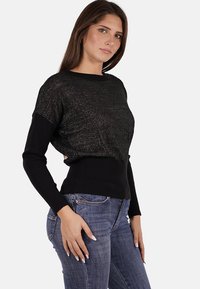 Maglione nero con una texture luccicante, orlo a coste e maniche lunghe, abbinato a jeans blu. Design semplice e aderente.