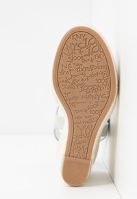Semelle d'une chaussure de couleur claire montrant une semelle extérieure en caoutchouc texturée avec des mots embossés incluant "DKNY," "New York," et "100%."