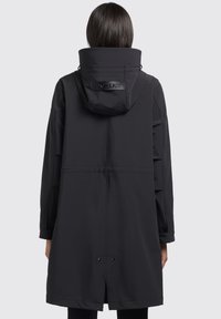 Cappotto esterno nero con cappuccio, maniche lunghe e texture liscia. Presenta un'etichetta con il marchio sul colletto e una fessura sul retro per la ventilazione.