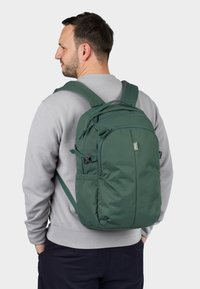 Zelený batoh s elegantním designem, vyrobený z odolné tkaniny. Obsahuje několik kapes, nastavitelné popruhy a značkovou etiketu.