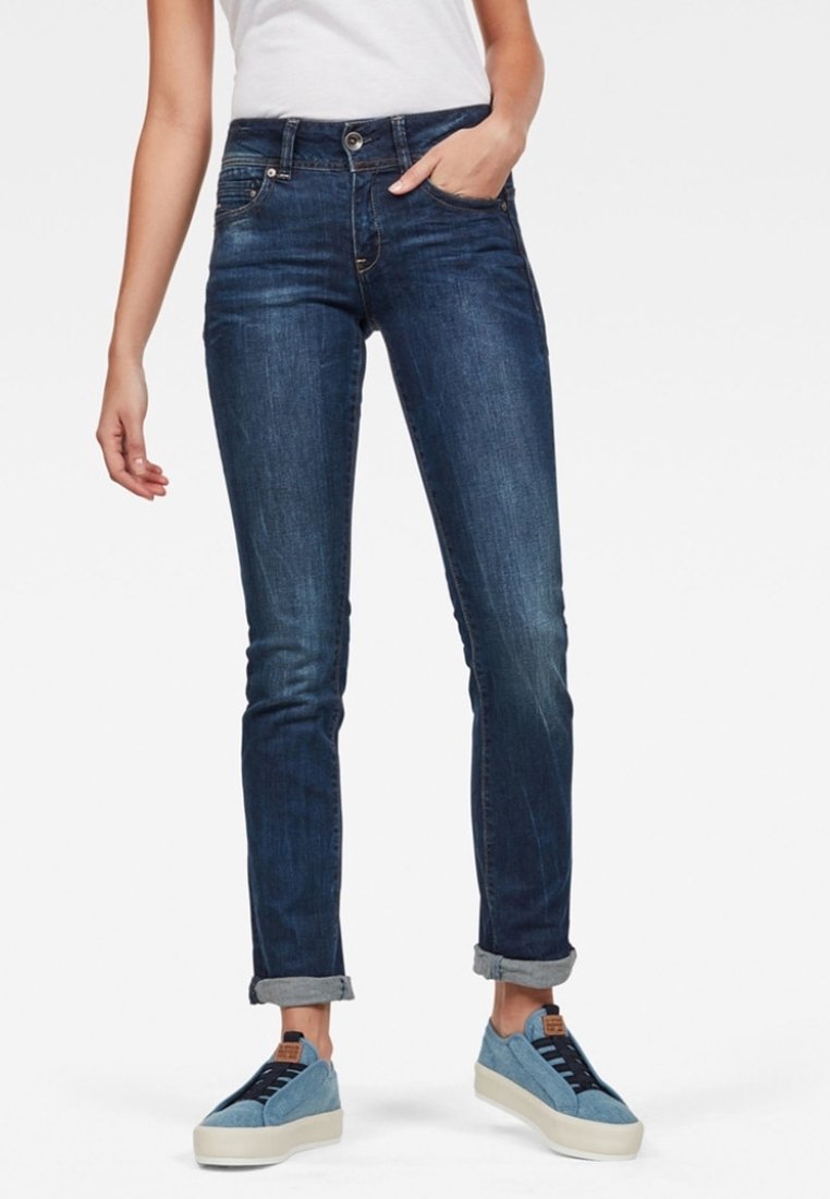 Mörkblå denimjeans med en figursydd passform, som har fem fickor och upprullade fållar. Tillsammans med ljusblå sneakers.