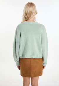 Myntgrön stickad tröja med sänkt axel, ribbad nederkant och långa ärmar, kombinerad med en brun mocka minikjol. Ingen framträdande mönster.