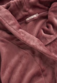 Fleecejacka i mjuk mauve-rosa, med en slät textur och en avslappnad huva. Dragkedja framtill och etikett synlig längs med halslinningen.